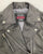 A close up of the collar on this classic black leather jacket with epaulets on the shoulders, high collar, zipped cuffs, adjustable belt, multiple pockets and a silver satin effect lining.