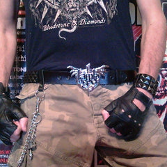 An 80's Metal black leather belt featuring 3 rows of black pyramid studs and a silver Lamb of God Wrath buckle.